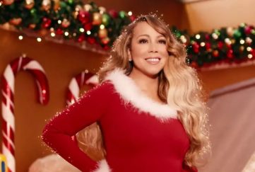 Image capture from Mariah Carey's updated music video for All I Want For Christmas, 2019. Features Mariah in front of a Christmas backdrop wearing a Santa suit and surrounded by sparkles. The song is a Christmas Number One Contender for 2023.