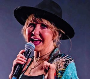 5 reasons we love lulu! Image features Lulu performing on stage at Fringe By The Sea. She's wearing a black trilby hat, a beautiful blue and leopard print kimono and layered necklaces.