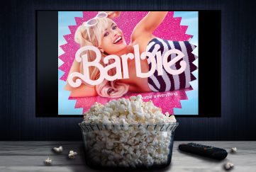 2024 baby names will be heavily influenced by what's on our screens, including the 'Barbie' movie! Image feature a Barbie movie promo shot of Margot Robbie playing on a TV screen. In the foreground is a bowl of popcorn and TV remote on the table.