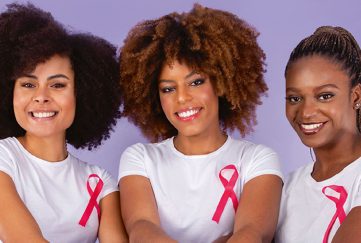 Three women wearing white t-shirts with pink ribbon for breast cancer charity