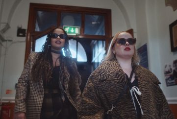 Screengrab from Channel 4's 'Big Mood', starring Nicola Coughlan (Bridgerton) and Lydia West (Inside Man). the pair are wearing leopard print coats and shades while strutting through the dront doors and down the hall of their old secondary school. Best New TV Shows April.