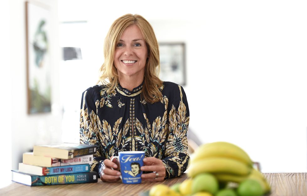 Bestselling author Adele Parks sitting at a desk with cup and books