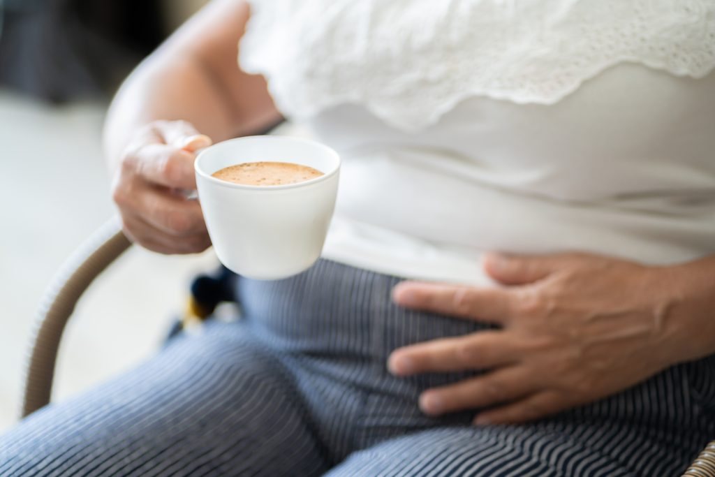 Woman holding coffee cup and holding stomach.