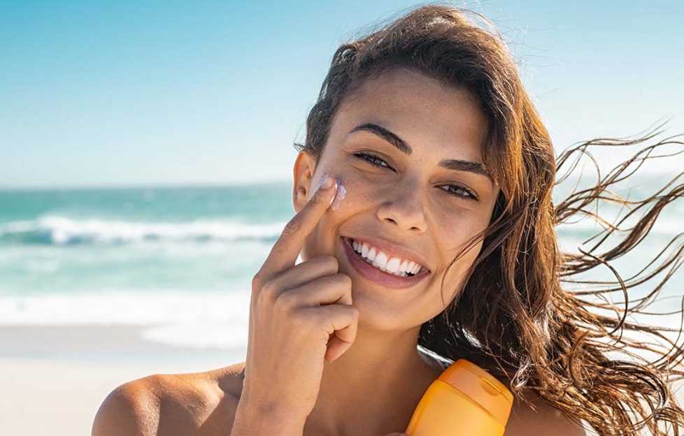 A lady at beach applying sunscreen to face