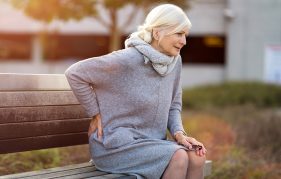 An older lady on park bench holding a painful back