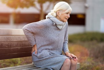 An older lady on park bench holding a painful back